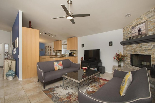 living room with light tile patterned floors, ceiling fan, track lighting, and a stone fireplace