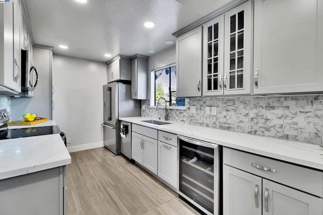 kitchen with sink, gray cabinets, light stone counters, stainless steel appliances, and beverage cooler