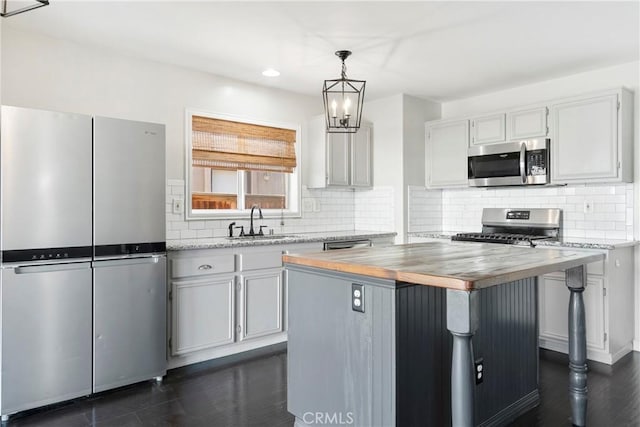 kitchen featuring butcher block counters, sink, hanging light fixtures, a kitchen island, and appliances with stainless steel finishes