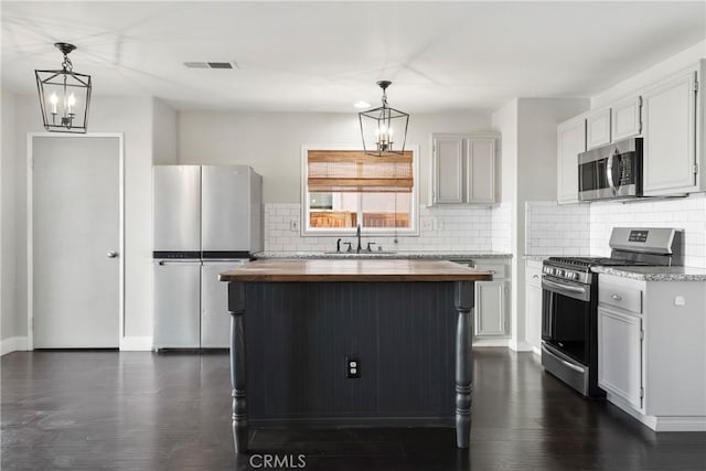 kitchen with wood counters, stainless steel appliances, sink, decorative light fixtures, and a center island