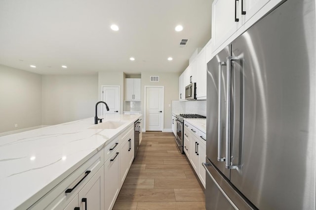 kitchen featuring light stone countertops, sink, light hardwood / wood-style flooring, high quality appliances, and white cabinets