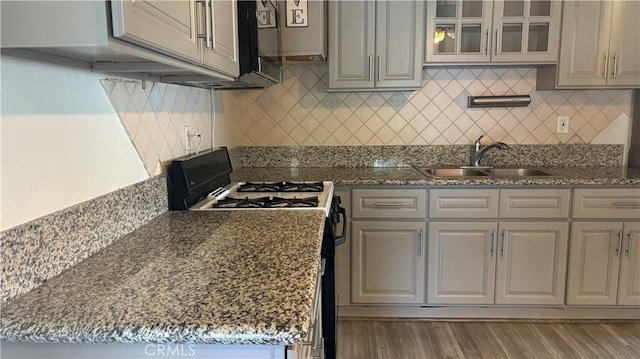 kitchen with hardwood / wood-style floors, sink, gas range, decorative backsplash, and stone countertops