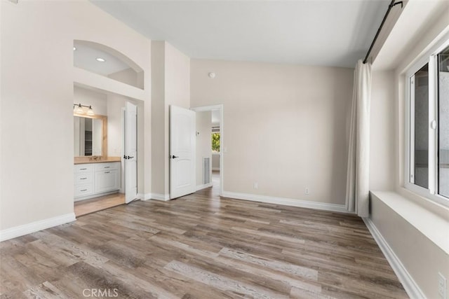 unfurnished bedroom featuring high vaulted ceiling, light hardwood / wood-style floors, and connected bathroom