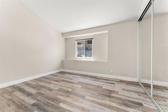 unfurnished bedroom with light hardwood / wood-style floors, vaulted ceiling, and a closet