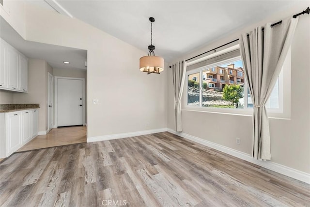 unfurnished dining area featuring light wood-type flooring and vaulted ceiling