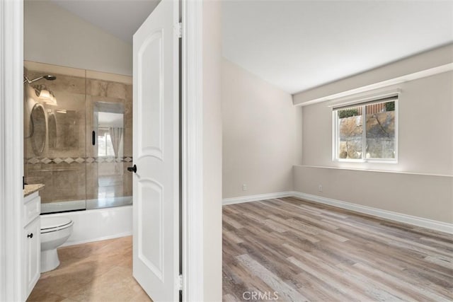 interior space featuring bath / shower combo with glass door, vanity, vaulted ceiling, hardwood / wood-style floors, and toilet