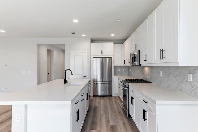 kitchen with white cabinets, a center island with sink, sink, appliances with stainless steel finishes, and light hardwood / wood-style floors