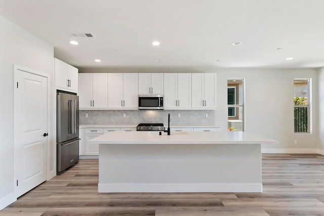 kitchen with white cabinets, premium appliances, light hardwood / wood-style floors, and a kitchen island with sink