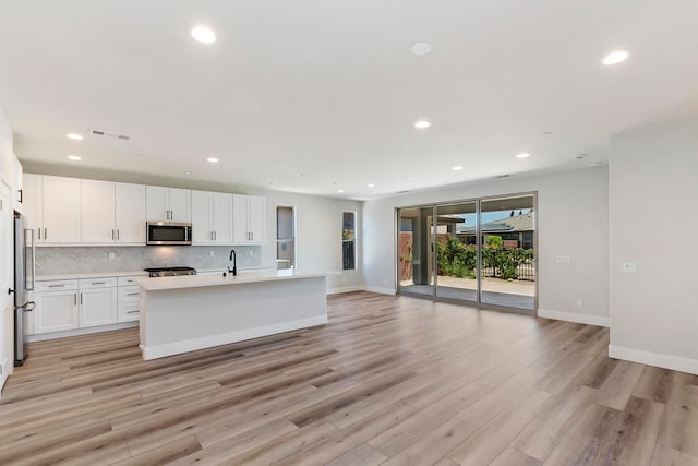 kitchen with white cabinets, light hardwood / wood-style floors, stainless steel appliances, and an island with sink