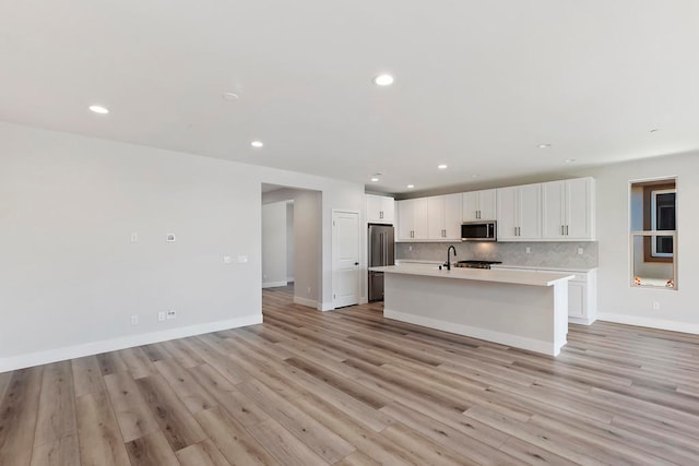 kitchen featuring a kitchen island with sink, white cabinets, decorative backsplash, light wood-type flooring, and appliances with stainless steel finishes