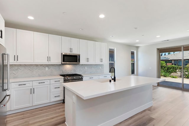 kitchen with high end appliances, white cabinets, sink, light wood-type flooring, and an island with sink