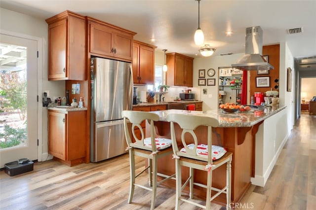 kitchen featuring island range hood, a kitchen breakfast bar, hanging light fixtures, light hardwood / wood-style floors, and stainless steel refrigerator