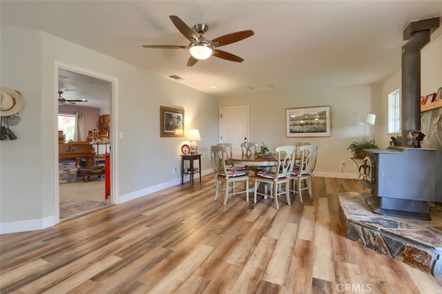 dining space featuring a wood stove, ceiling fan, and light hardwood / wood-style floors