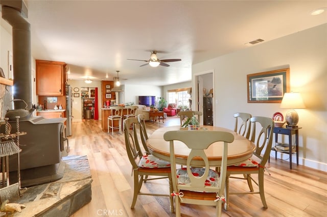 dining room featuring a wood stove, ceiling fan, and light wood-type flooring