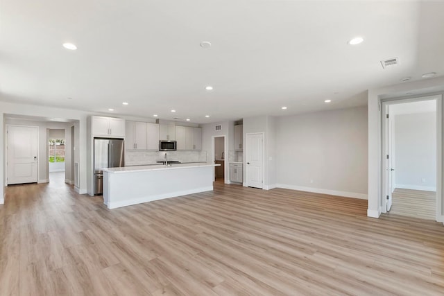 kitchen featuring decorative backsplash, light wood-type flooring, stainless steel appliances, a kitchen island with sink, and white cabinets