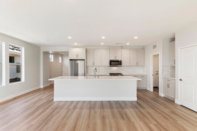 kitchen featuring white cabinetry, tasteful backsplash, a center island with sink, appliances with stainless steel finishes, and light wood-type flooring