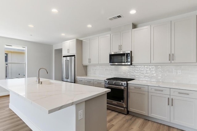 kitchen with a kitchen island with sink, sink, stainless steel appliances, and light wood-type flooring