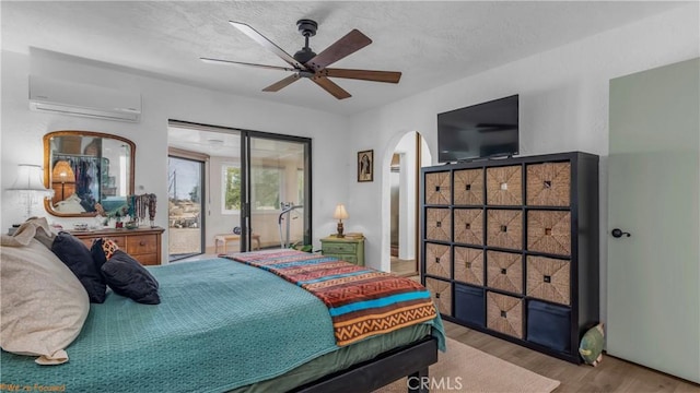 bedroom featuring arched walkways, a ceiling fan, a wall unit AC, wood finished floors, and access to exterior