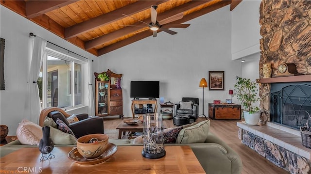 living area with a fireplace with raised hearth, a ceiling fan, lofted ceiling with beams, wood ceiling, and light wood-style floors