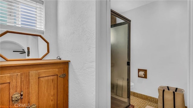 bathroom with toilet, a stall shower, and a textured wall