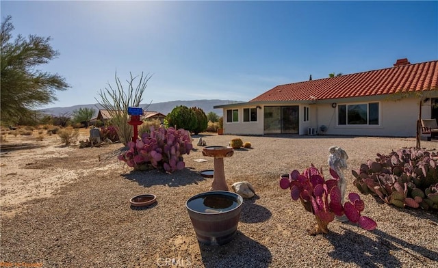 back of property with a chimney, a tile roof, a mountain view, and stucco siding