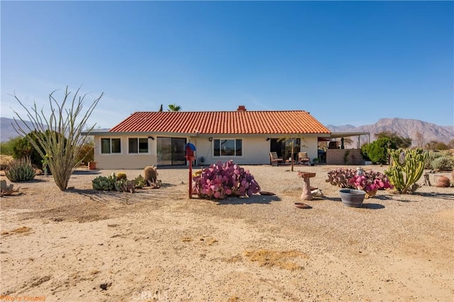 back of property with a tiled roof, a chimney, a mountain view, and stucco siding