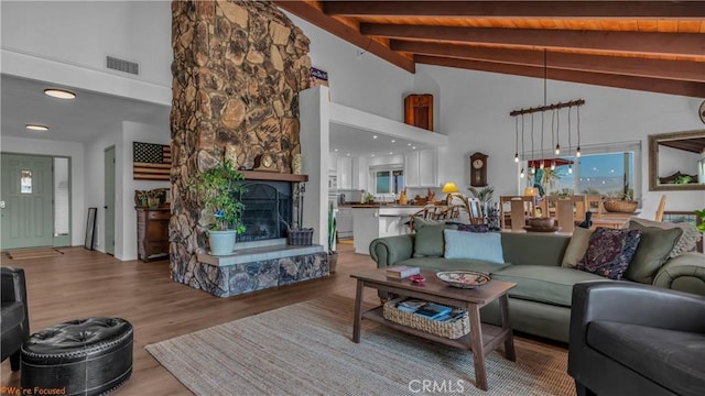 living room with beam ceiling, a fireplace, light wood finished floors, visible vents, and high vaulted ceiling