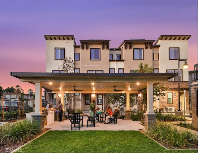 back house at dusk featuring a lawn, area for grilling, ceiling fan, and a gazebo