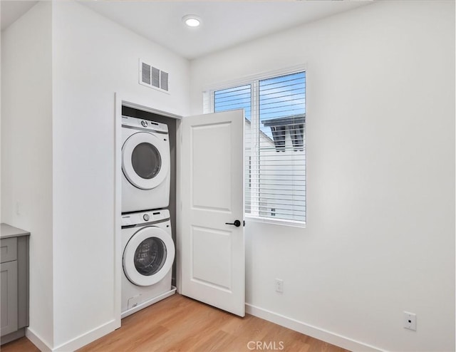 laundry room with light wood-type flooring and stacked washer / drying machine