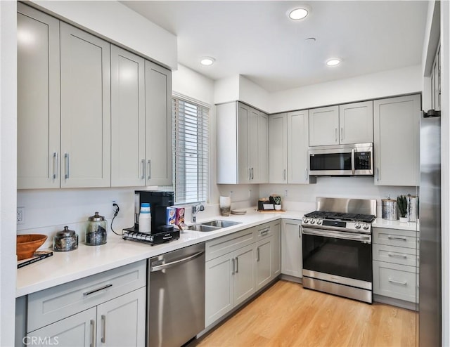 kitchen with appliances with stainless steel finishes, light wood-type flooring, gray cabinets, and sink