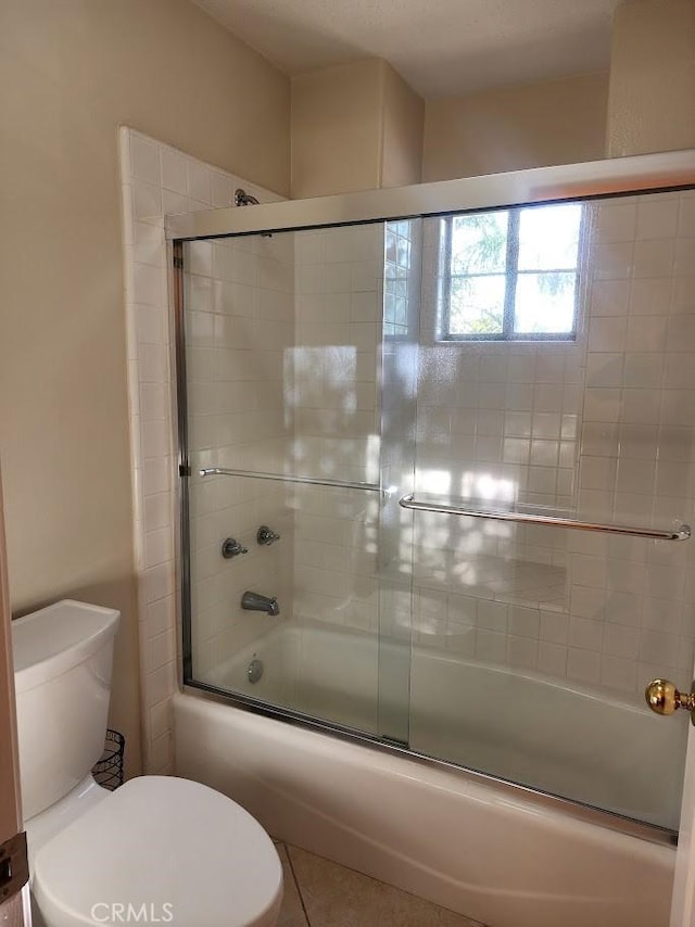 bathroom featuring tile patterned floors, toilet, and shower / bath combination with glass door