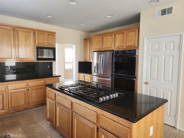 kitchen featuring a kitchen island, tasteful backsplash, dark stone countertops, light tile patterned flooring, and black appliances