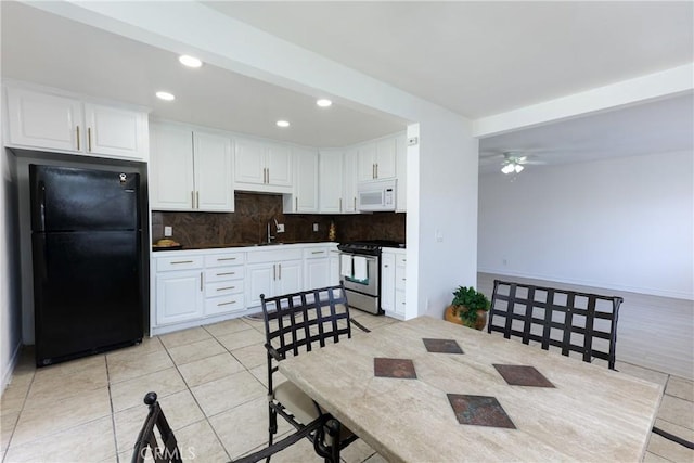 kitchen featuring white cabinets, decorative backsplash, ceiling fan, gas stove, and black fridge