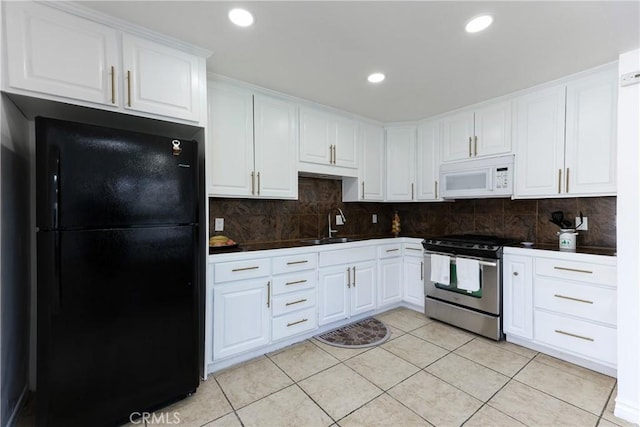 kitchen featuring stainless steel gas range oven, white cabinetry, tasteful backsplash, light tile patterned floors, and black refrigerator