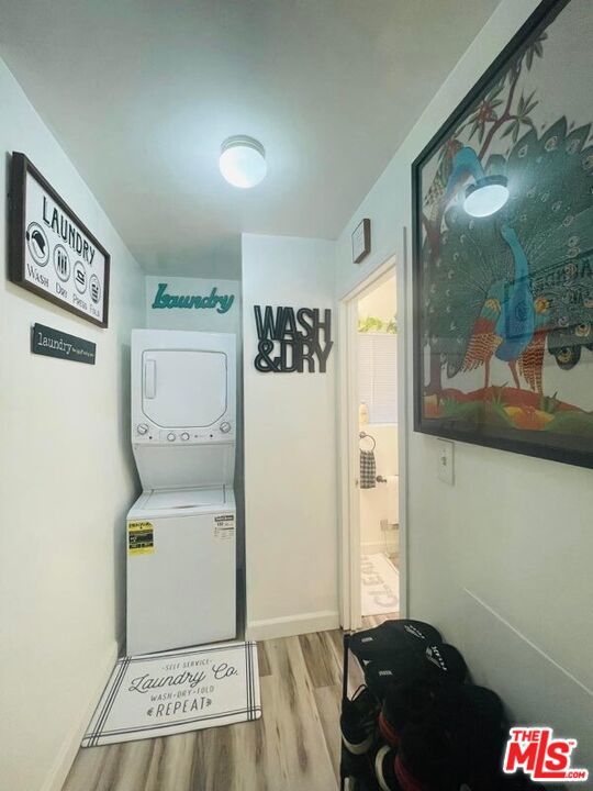 washroom with stacked washer / drying machine and light hardwood / wood-style flooring