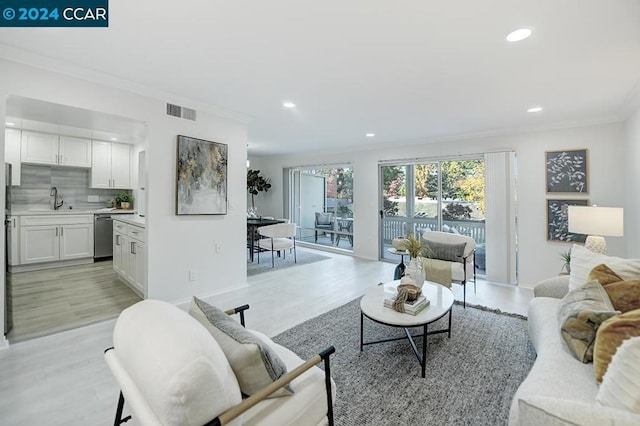 living room featuring ornamental molding, sink, and light hardwood / wood-style flooring