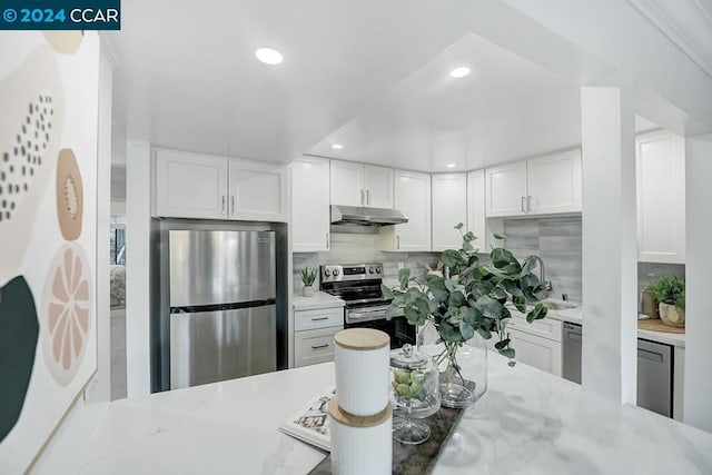 kitchen featuring white cabinetry, sink, light stone counters, backsplash, and appliances with stainless steel finishes