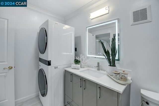 clothes washing area featuring stacked washer and dryer, ornamental molding, and sink