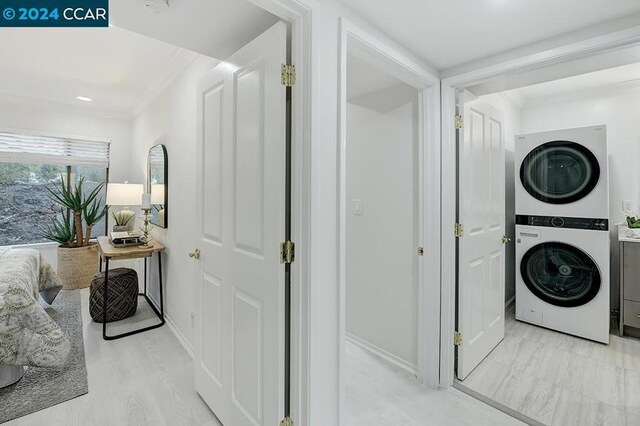 clothes washing area with stacked washing maching and dryer, light hardwood / wood-style flooring, and ornamental molding