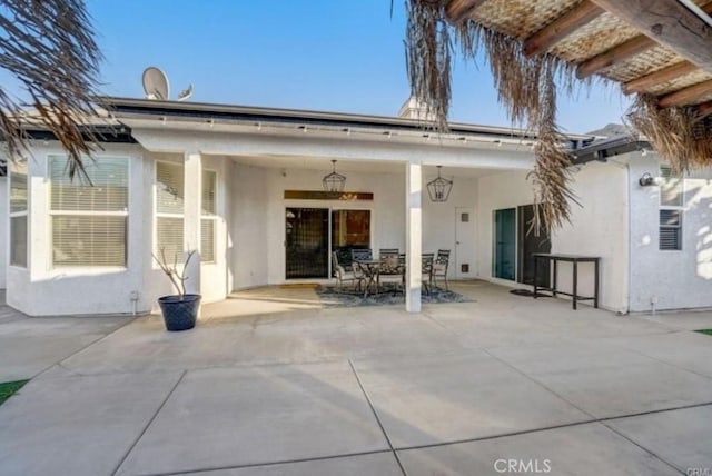 rear view of house with outdoor dining area, a patio area, and stucco siding