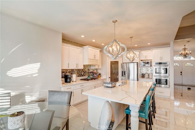 kitchen with white cabinetry, appliances with stainless steel finishes, backsplash, and a notable chandelier