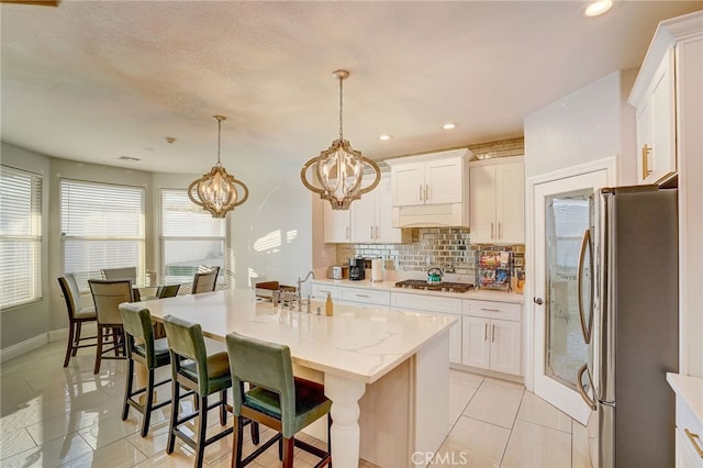 kitchen featuring stainless steel appliances, white cabinetry, an island with sink, and tasteful backsplash