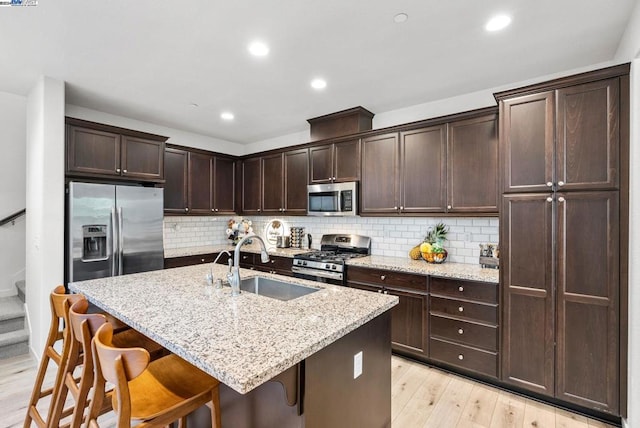 kitchen featuring a center island with sink, a kitchen breakfast bar, sink, light wood-type flooring, and appliances with stainless steel finishes