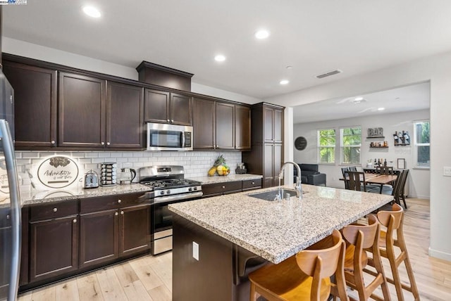 kitchen featuring sink, an island with sink, stainless steel appliances, and light wood-type flooring