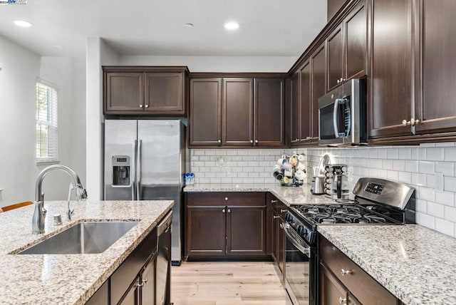 kitchen featuring light stone countertops, sink, decorative backsplash, appliances with stainless steel finishes, and light wood-type flooring