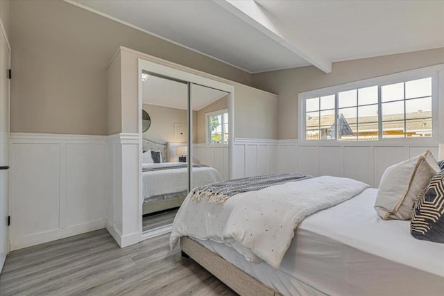 bedroom featuring vaulted ceiling with beams, light wood-type flooring, and a closet