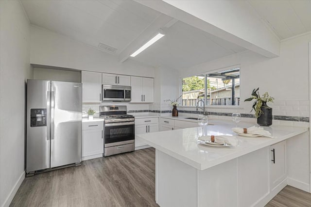 kitchen with vaulted ceiling with beams, kitchen peninsula, stainless steel appliances, light hardwood / wood-style floors, and white cabinets