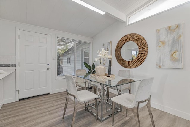 dining room with lofted ceiling with beams, a healthy amount of sunlight, and light wood-type flooring