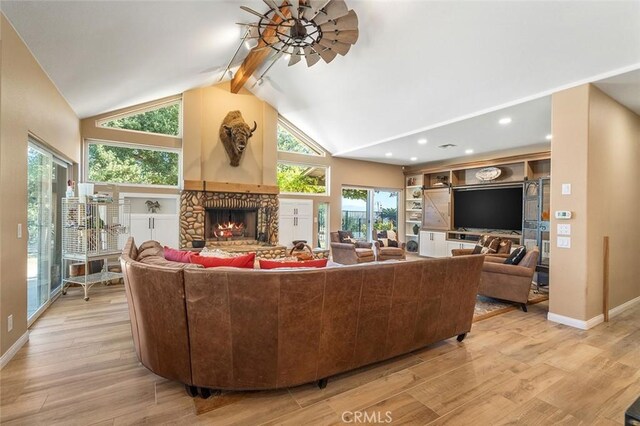 living room featuring ceiling fan, high vaulted ceiling, beamed ceiling, light hardwood / wood-style floors, and a stone fireplace