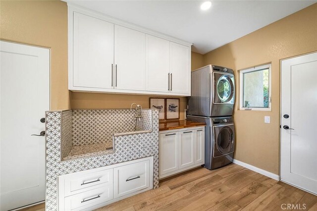 laundry area featuring stacked washer / dryer, cabinets, and light hardwood / wood-style floors